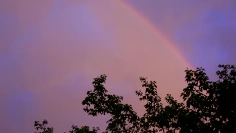 Regenbogen-am-bewölkten-Himmel-über-Stadtbild-am-Abend-bei-Sonnenuntergang.