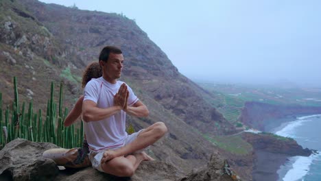 Mann-und-Frau-sitzen-auf-einem-Berg-auf-einem-Felsen-zurück-zu-meditieren-und-Yoga-auf-dem-Hintergrund-des-Ozeans-zu-tun.