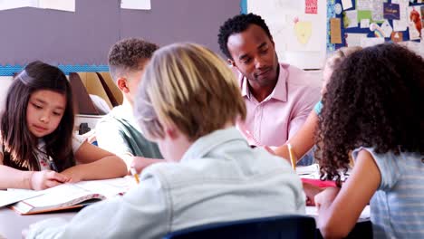 Lehrer-arbeiten-mit-Kindern-der-Grundschule-an-ihrem-Schreibtisch