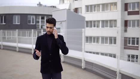 Serious-handsome-young-businessman-communicating-on-smartphone-smiling-confident.