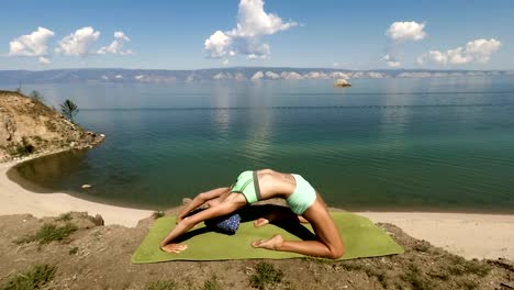 Mujer-haciendo-yoga-en-la-estera-del-ejercicio-cerca-de-lago-azul.