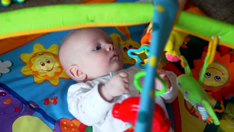 Kleines-Baby-spielt-mit-Spielzeug-auf-Mat