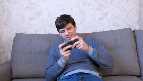 Man-is-playing-game-on-his-mobile-phone-sitting-on-the-sofa.