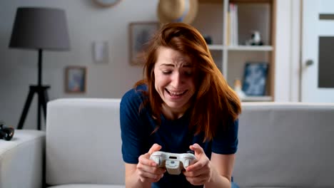 Chica-decidida-jugando-un-videojuego-en-casa.-Mujer-jugadora-excitada-sentada-en-un-sofá,-jugando-y-perdiendo-en-videojuegos-en-una-consola,-usando-un-mando-inalámbrico.-Habitación-acogedora,-ambiente-casero-encantador