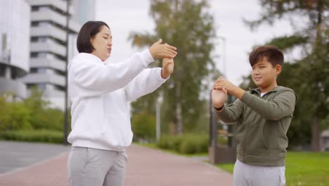 Muñecas-asiáticas-de-estiramiento-de-mujer-y-niño-durante-el-entrenamiento-al-aire-libre