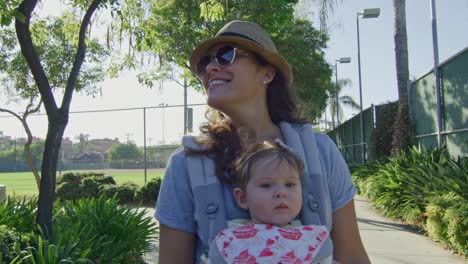 Woman-with-a-baby-in-carrier-smiling-as-she-walks-at-a-park