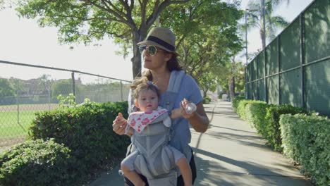 Mujer-sonriendo-mientras-camina-con-el-bebé-en-el-portaequipajes-en-un-parque