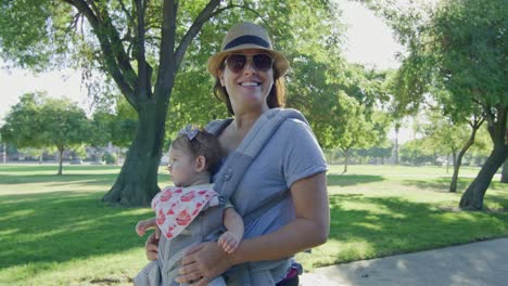 Happy-woman-walking-on-a-park-carrying-her-baby-on-carrier