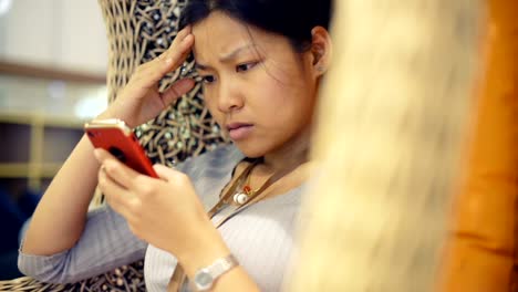 Discouraged-Thai-Girl-sits-in-wicker-chair-reading-phone