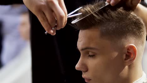 Hairstylist-cuts-hair-of-young-man-with-scissors