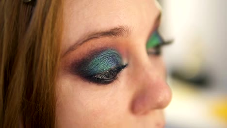 Close-up-of-young-female-model-is-being-maked-up-in-studio.-Artist-is-applying-black-liner-to-lower-lid-of-the-right-eye-using-a-brush.-Side-view