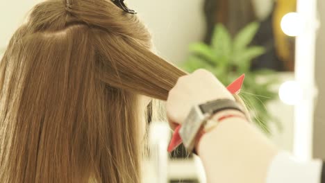 Female-hairdresser-using-hair-tongs-and-comb-for-hair-straightening-in-beauty-salon.-Close-up-hairstylist-straightening-female-hair-during-hairstyling-in-hairdressing-salon