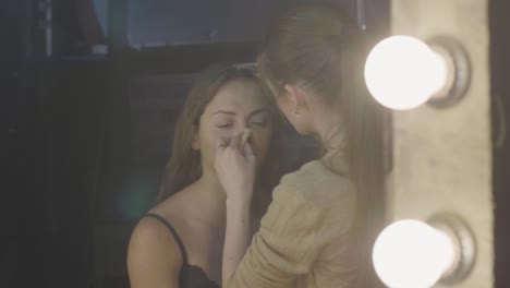 Artista-de-maquillaje-aplicando-crema-de-base-en-la-cara-de-piel-mientras-que-la-mujer-se-componen