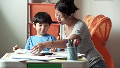 Children-homework.-Young-mixed-race-boy-doing-homework-in-terrace-at-home.-Reading-book-with-his-mother.-Happy-mood.-Back-to-school-concept.