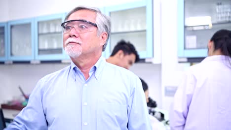 Scientists-working-in-lab-portrait.-Senior-chinese-male-scientist-working-in-lab-with-VR-glasses-pressing-the-button-portrait-with-his-team-in-background.-For-special-effect-overlay.