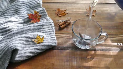 Pouring-water-to-cup-with-a-tea-bag-on-a-wooden-table-with-colored-autumn-leaves---slow-motion