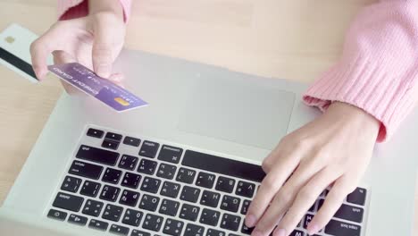 Beautiful-Asian-woman-using-computer-or-laptop-buying-online-shopping-by-credit-card-while-wear-sweater-sitting-on-desk-in-living-room-at-home.-Lifestyle-woman-at-home-concept.