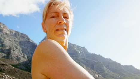 Senior-woman-standing-with-arms-outreached-at-countryside