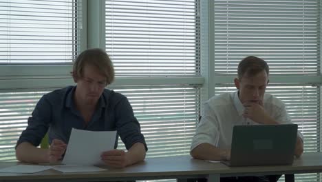Zwei-thinkful-Männer-sitzen-am-Tisch-im-Büro