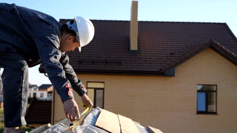 Adult-professional-builder-in-hardhat-measuring-length-of-wood-lumber-on-site-under-blue-sky,-slow-motion