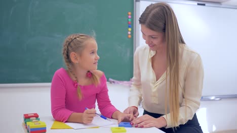 Nachhilfe,-weibliche-Erzieher-hilft,-Gelehrter-Mädchen-beschaffen-Informationen-über-Kunststoff-Figuren-am-Tisch-in-der-Nähe-Tafel-im-Klassenzimmer-der-Schule