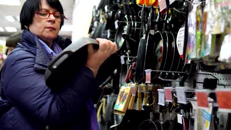 Eine-reife-Frau-wählt-eine-gusseiserne-Pfanne-im-Supermarkt.