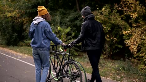 Schöne-junge-Paar-umarmt,-beginnend-mit-Fahrrädern-im-Stadtpark-im-Herbst-Park-zu-gehen.-Konzept-der-aktiven-Lebensstil,-Kommunikation,-dating.-Seltener-Blick