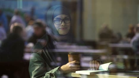 Young-Arabic-female-student-reading-book-in-cafe,-preparing-for-test