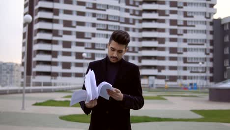 Attractive-young-businessman-in-black-suit-throw-out-documents-outdoor-against-office-building.