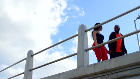 Happy-couple-interacting-with-each-other-while-walking-near-railing-4k