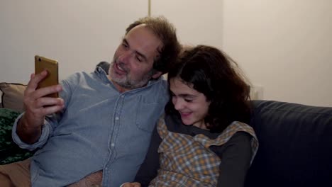 Happy-dad-and-daughter-sitting-on-couch-and-having-video-chat