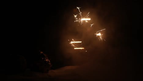 Glittering-burning-sparkler-on-snow-with-blurred-Christmas-tree-on-dark-background.-New-Year-Holiday-concept-with-empty-space-for-your-text.-Selective-focus