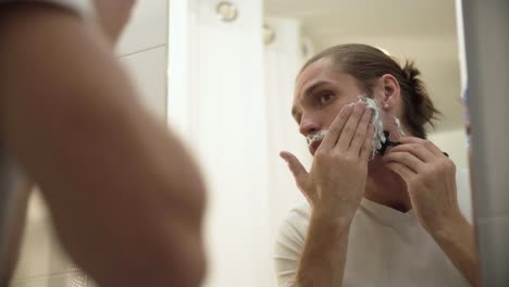 Man-Shaving-Beard-With-Razor-In-Bathroom