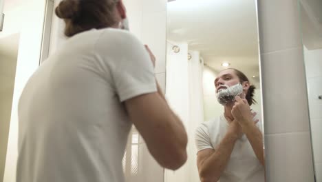 Man-Shaving-Beard-With-Razor-In-Bathroom