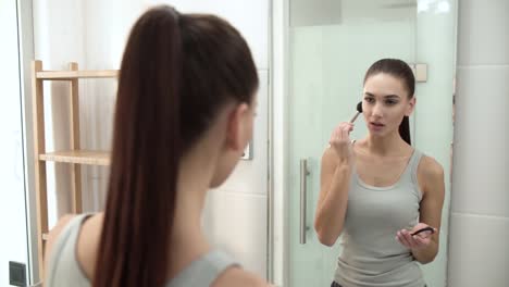 Maquillaje-de-la-cara.-Mujer-usando-polvo-y-mirando-en-el-espejo