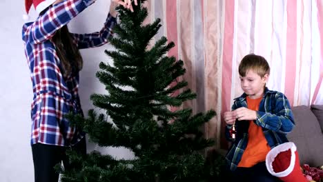 Mamá-e-hijo-en-sombreros-de-Navidad-decorar-árbol-de-Navidad-con-cuentas-y-bolas.