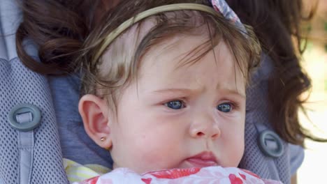 Close-up-of-a-baby-with-blue-eyes-while-on-mother's-carrier