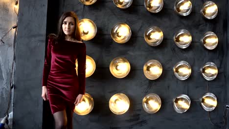 Young-girl-in-dress-and-beautiful-face-on-a-background-of-wall-with-powerful-lamps