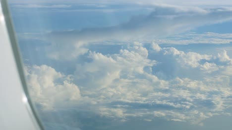 Big-white-heap-clouds-on-blue-sky-looking-through-airplane-porthole.