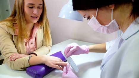 beautician-filing-nails-to-customer-in-beauty-salon