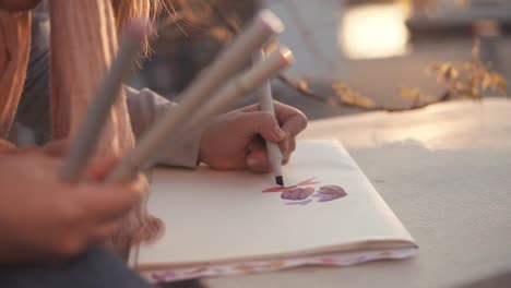 Girl-is-drawing-outdoors-in-park,-close-up-of-hands-with-markers-and-picture
