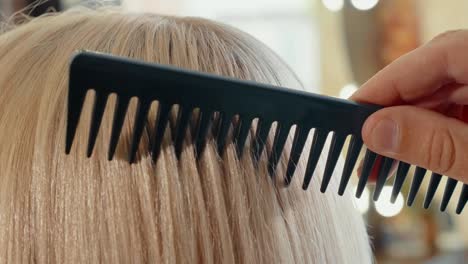 Male-hairdresser-combing-hair-to-blonde-girl-in-beauty-salon,-close-up