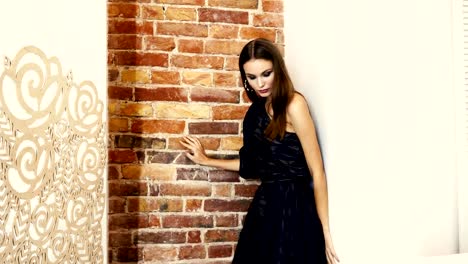 demonstration-of-a-new-collection-of-clothes,-striking-brunette-with-dark-makeup-in-evening-dress-on-one-shoulder-poses-for-photo-shoot-on-background-of-brick-wall