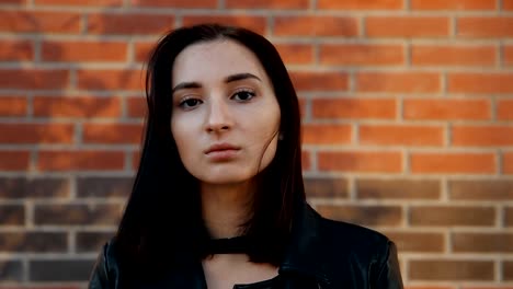 Portrait-of-a-young-serious-sexy-woman-against-a-brick-wall.-Slow-motion-shot.