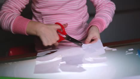 Close-up-shot-of-preschool-girl-hands-in-pink-sweater-cutting-shapes-from-paper-with-scissors-and-drawing-with-a-pencil