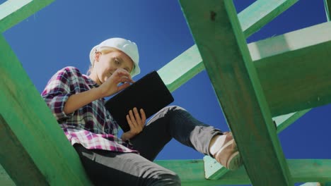 Low-angle-video:-engineer,-works-among-the-rafters-of-the-roof,-uses-a-tablet.-Technical-control-in-construction