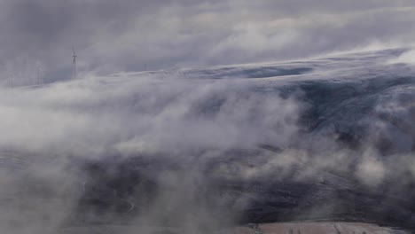 low-clouds-drifting-besides-mountains-during-sunrise,-showing-windmills-in-the-scotland