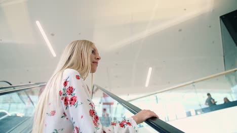 Joven-mujer-rubia-montar-en-escalera-eléctrica