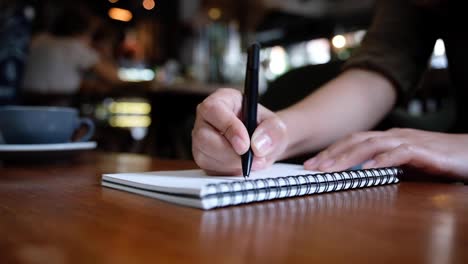 Lenta-de-la-mano-de-una-mujer-escribiendo-en-cuadernos-en-blanco-de-madera-mesa-de-café