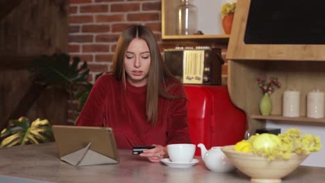 Young-woman-making-purchase-online,-typing-credit-card-details-on-tabletPC-in-the-modern-kitchen